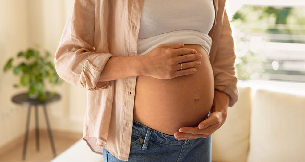 Eine Person, die vermutlich schwanger ist, berührt sanft ihren Bauch.
